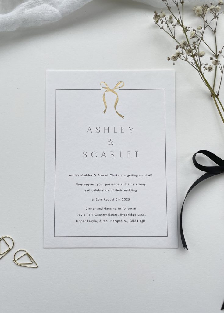 Luxury wedding invitation with a gold foil bow set within a black border with modern type, perfect for contemporary weddings