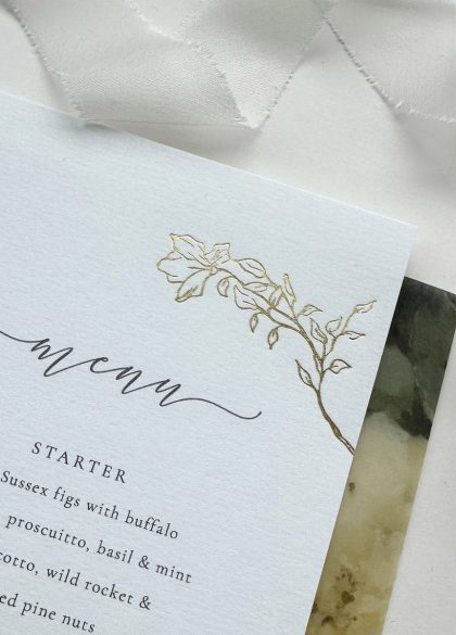 Close-up of a gold foil rose wedding menu showcasing delicate vintage inspired floral foil detailing on luxurious white card.