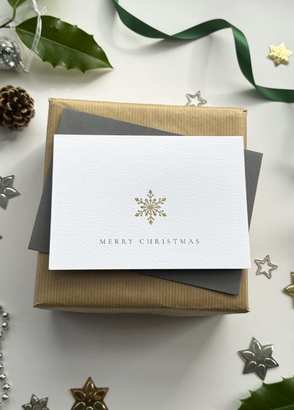 Elegant Merry Christmas card featuring a minimalist gold foil snowflake design, styled with holly and ribbon.