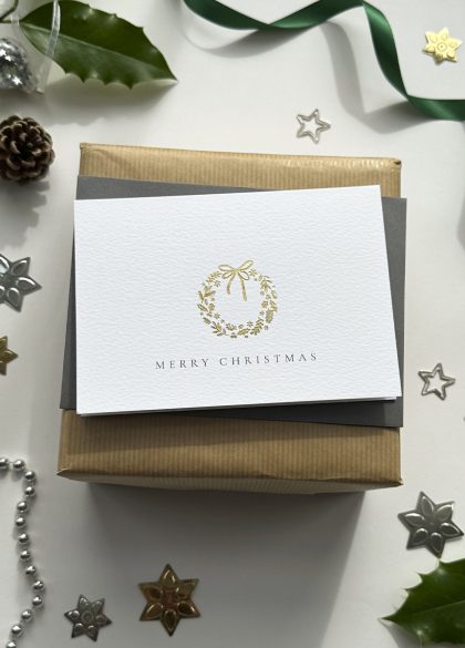 Stylish gold foil luxury Christmas card with wreath illustration and Merry Christmas message, flat lay holiday stationery scene.