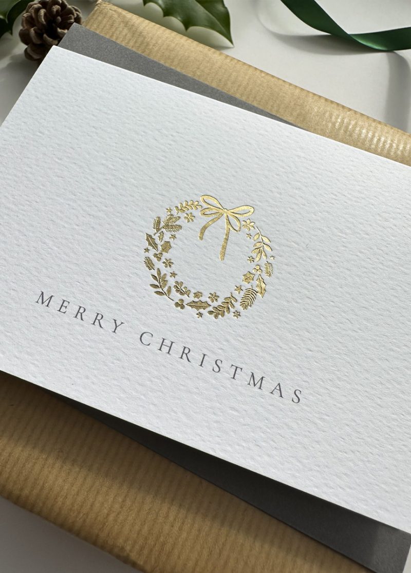 Minimalist gold foil wreath Christmas card with fine typography and premium cardstock, styled with festive stars and holly.