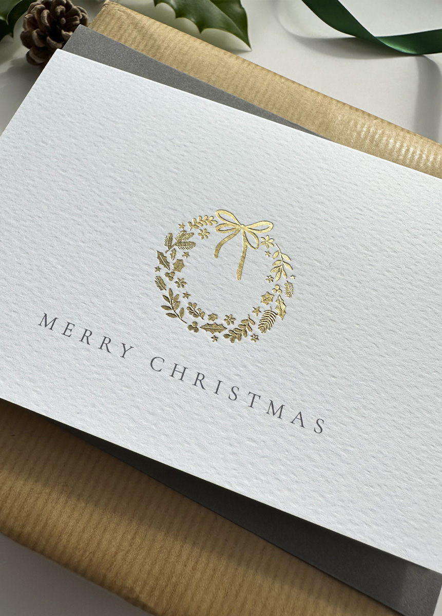 Minimalist gold foil wreath Christmas card with fine typography and premium cardstock, styled with festive stars and holly.