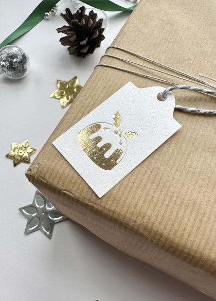 Gold foil Christmas pudding tag tied on brown paper gift with pinecone and holly decoration
