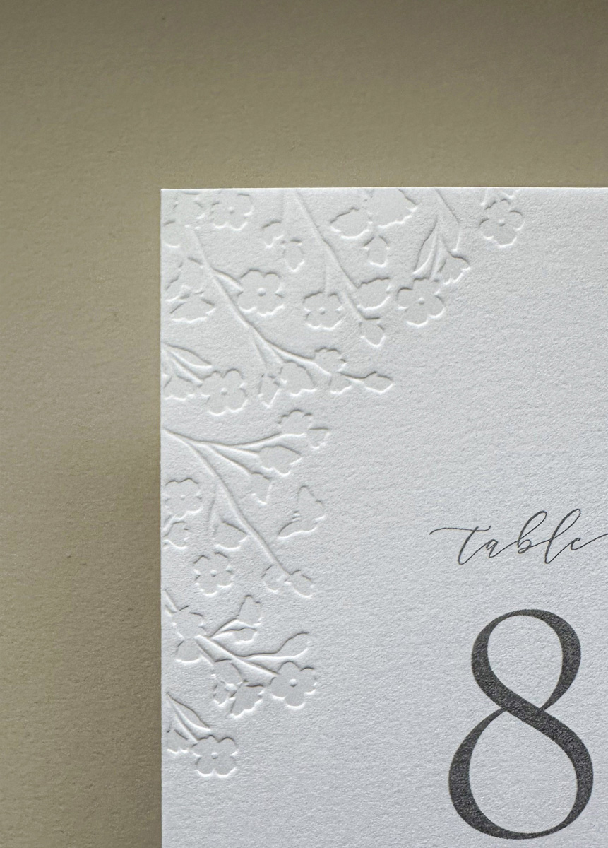 Luxury reception table number with raised floral embossing and elegant typography printed on textured cotton card.