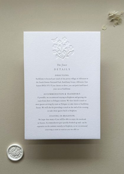 Minimalist wedding information card with embossed floral details and refined typography on luxury white cotton card.