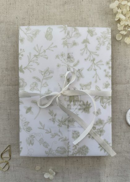 Luxury pure silk ribbon tied around a floral embossed wedding invitation suite with vellum wrap and wax seal.