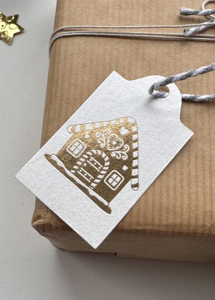 Close-up of the gold foil gingerbread house design on pearlescent Christmas gift tags.